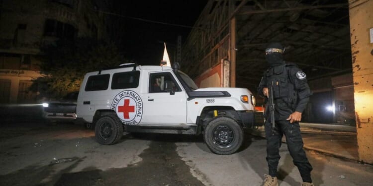 A gunman wearing the uniform of the al-Qassam Brigades, the military wing of Hamas, stands guard as Red Cross vehicles enter a warehouse allegedly to collect coffins containing the bodies of four deceased hostages in Gaza City on Tuesday.