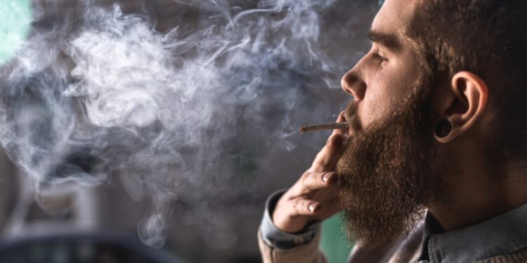 A close up of hipster man smoking weed cigarette.