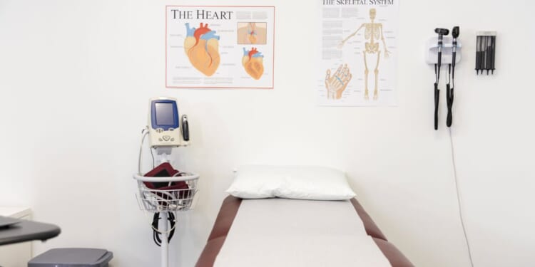 A clean, empty room in a doctor's office with an examination table and various pieces of medical equipment.