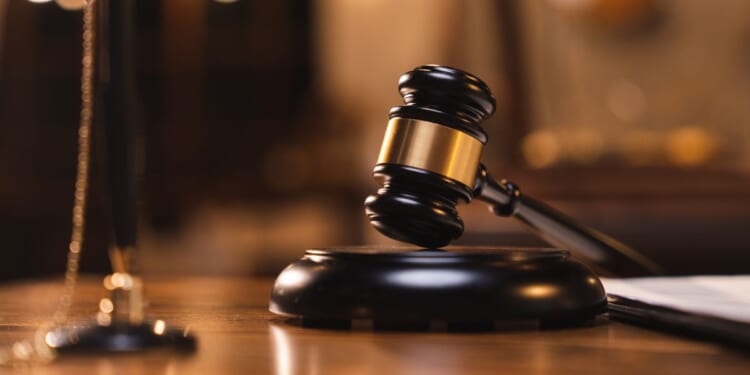 A judges gavel sits on a table as books sit in the background.