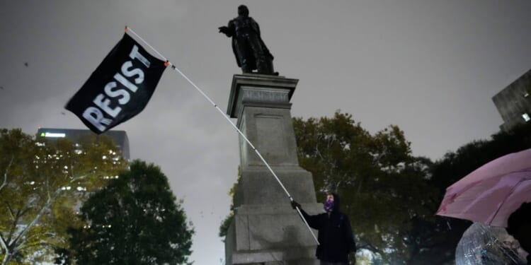 A protestor waves a flag in a pouring rain during a demonstration against an impending Customs and Border Patrol immigration crackdown in New Orleans on Dec. 1, 2025.