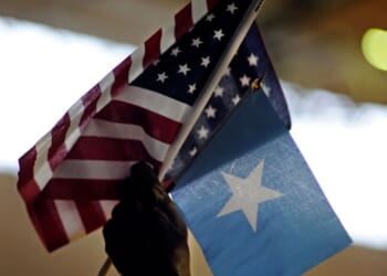Saeed Fahra holds high U.S. and Somali flags as he speaks to a mostly young male audience during a break in the action of Somali Week's Hoops for Hope basketball tournament at the Richard Green Central Park Community School gym on June 26, 2011, in Minneapolis, Minnesota.