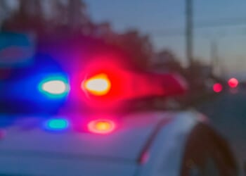 Police lights flash on top of a police car at night near a crime scene.