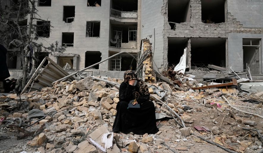 A woman sits on rubble across from a residential building damaged last Monday during the U.S.-Israeli air campaign in Tehran, Iran, Thursday, March 12, 2026. (AP Photo/Vahid Salemi)