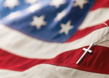 A Christian cross neckless is laid across an American flag.