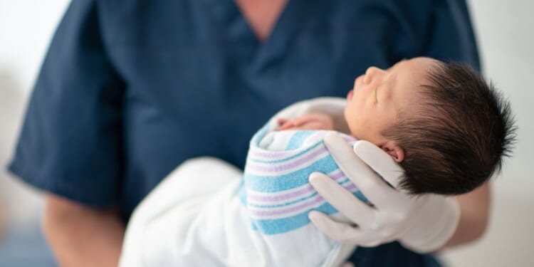 A nurse holds a newborn baby at a hospital as the child sleeps.