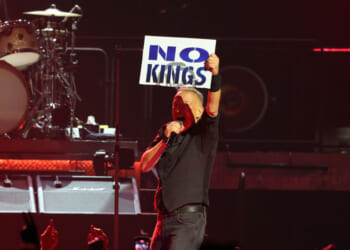 Bruce Springsteen, in concert, holding up a "No Kings" sign.