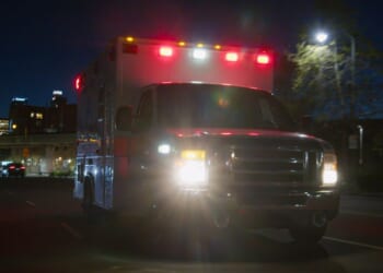 An ambulance driving through a downtown district at night.