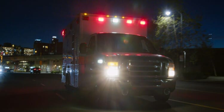 An ambulance driving through a downtown district at night.