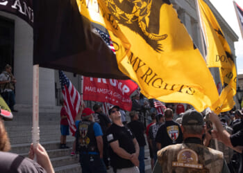 Gun rights activists stand with multiple flags at the Ohio Capitol, with the yellow 'Don't Tread on Me' flag prominently displayed.