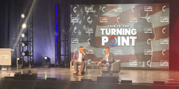 Lawrence Jones and Vivek Ramaswamy are seated in chairs on a stage with a Turning Point backdrop behind them.