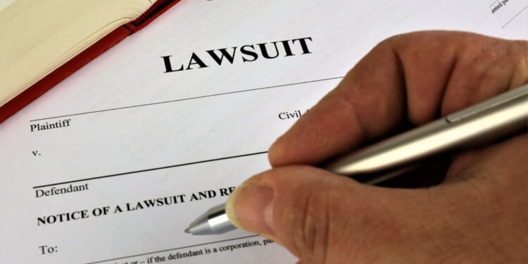 A man's hand readies a pen to begin filling out a lawsuit.