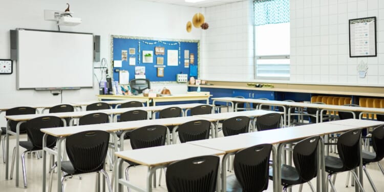 Chairs and desks sitting in rows in front of a whiteboard in a school classroom with no students.