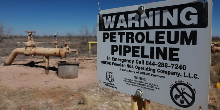 Yellow oil pipelines in a barren West Texas landscape. In the foreground, a sign reading "Warning Petroleum Pipeline"