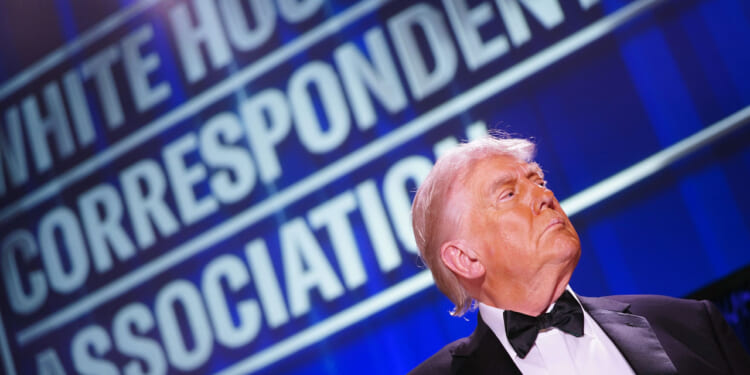 President Trump in profile in bottom right of shot underneath large "White House Correspondents' Dinner" sign.