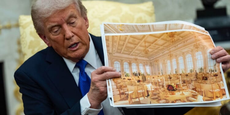 President Trump sits in the Oval Office on October 22, 2025 as he displays photos of the White House ballroom plans.