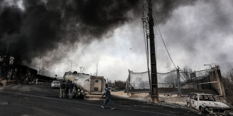 Dark smoke clouds engulf destroyed vehicles near an ongoing fire following an overnight airstrike on the Shahran oil refinery in northwestern Tehran.