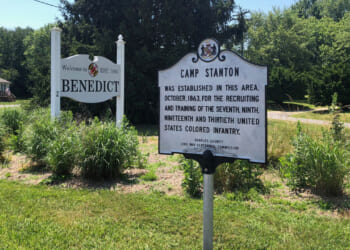 A grey historic marker for "Camp Stanton" alongside a welcome sign for Benedict.