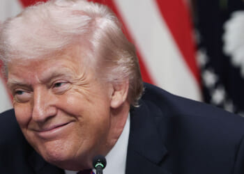 Close-up of Donald Trump grinning, with an American flag as a backdrop.