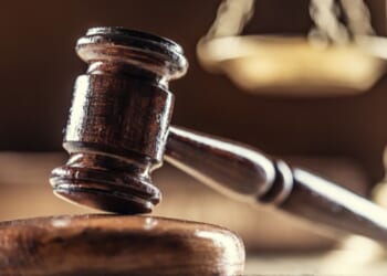A gavel lays on a wooden block next to a balancing scale in a dark room.