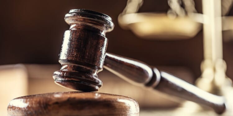 A gavel lays on a wooden block next to a balancing scale in a dark room.