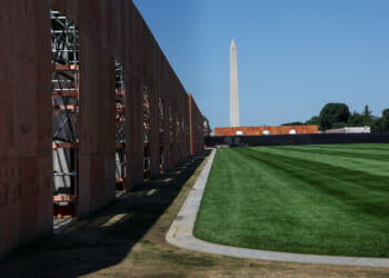 A temporary wooden fence surrounds a section of the National Mall, with the Washington Monument in the background.