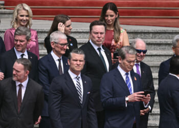 Pete Hegseth and Scott Bessent surrounded by business leaders including Elon Musk and Tim Cook stand on steps.