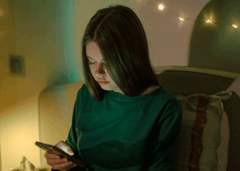Girl sits alone in her room with a phone in hand.