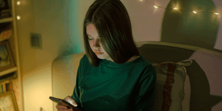 Girl sits alone in her room with a phone in hand.
