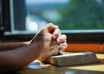 Hands in a prayerful position placed on a Bible.