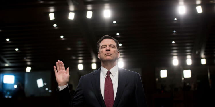 James Comey, with his eyes closed, raises right hand before giving congressional testimony.