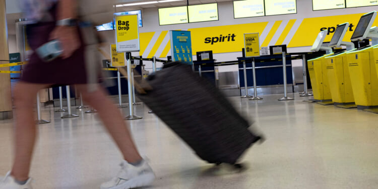 A woman drags her luggage past an empty Spirit Airlines counter at an airport.