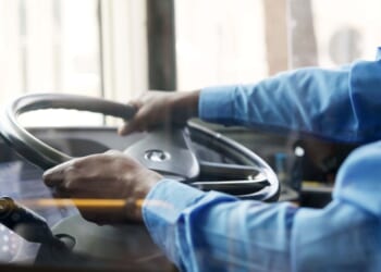 A bus driver holds the steering wheel of the bus with both hands.