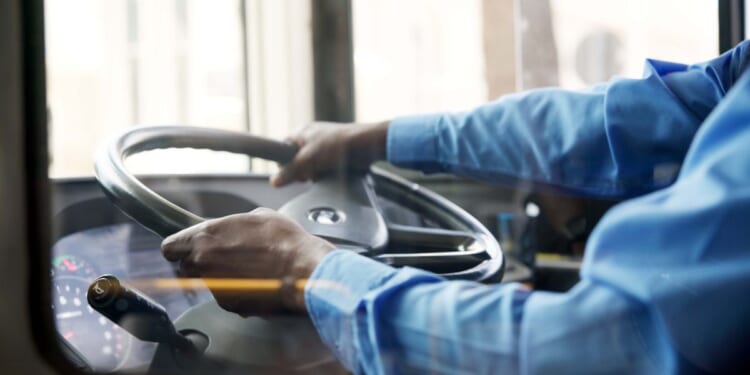 A bus driver holds the steering wheel of the bus with both hands.