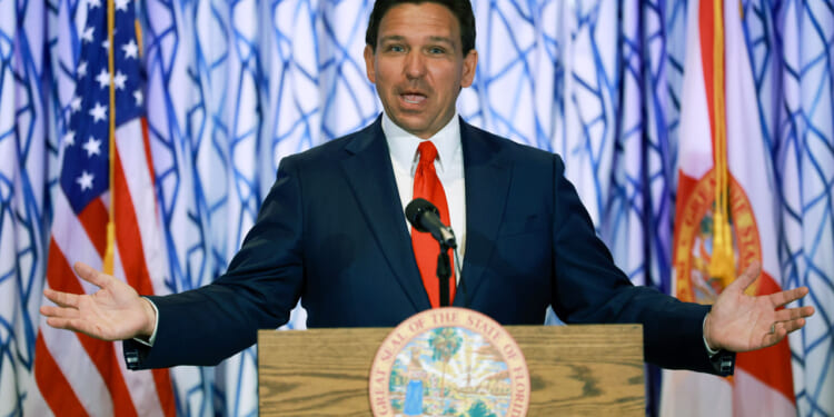 Ron DeSantis behind a podium with his mouth open and arms stretched wide.