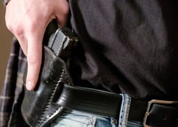 A man draws his gun from a leather holster on his belt.