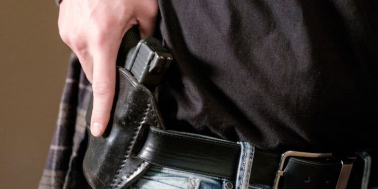 A man draws his gun from a leather holster on his belt.