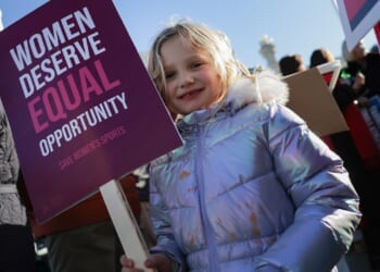 A young girl protests with a sign that says "Women deserve equal opportunity. Save women's sports."
