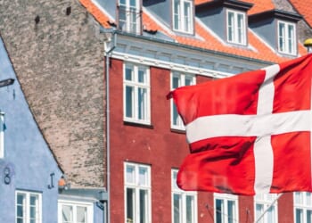 A Danish flag flies in front of traditional houses in Copenhagen.
