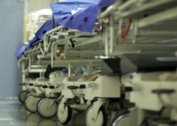 A hospital hallway is filled with gurneys and trolleys lined up on the wall.