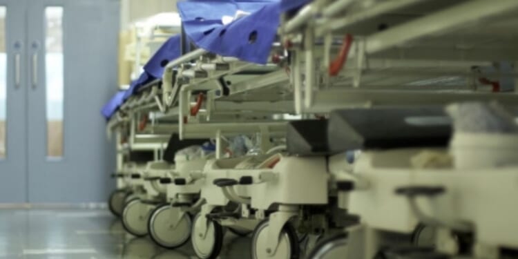 A hospital hallway is filled with gurneys and trolleys lined up on the wall.