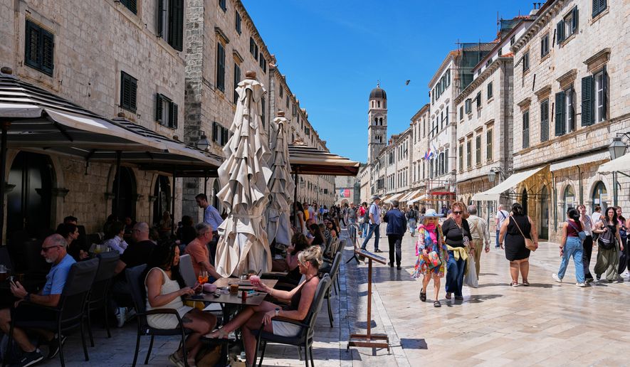 People sit in a cafe as others walk on the main street of Stradun in old town Dubrovnik, Croatia, Monday, April 27, 2026. (AP Photo/Darko Bandic)