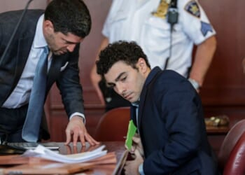 Luigi Mangione squirms in a New York courtroom while his lawyer speaks to him on May 18, 2026.