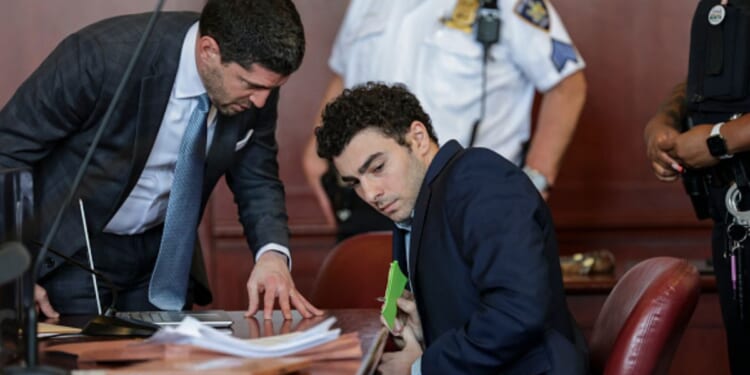 Luigi Mangione squirms in a New York courtroom while his lawyer speaks to him on May 18, 2026.