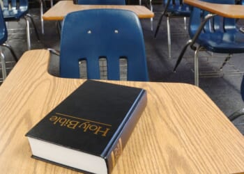 A bible sits on a school desk in a classroom.