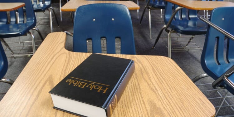 A bible sits on a school desk in a classroom.