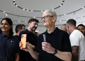 Apple CEO Tim Cook holding iPhones while surrounded by people