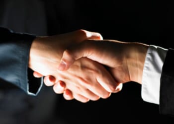 Two men shake hands in a dark room.