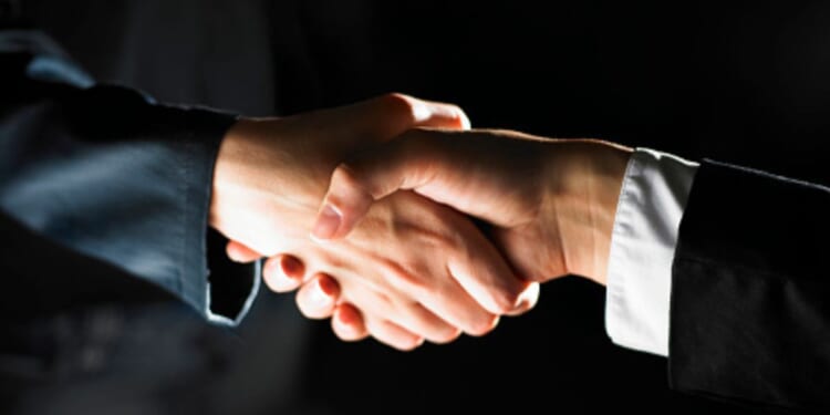 Two men shake hands in a dark room.