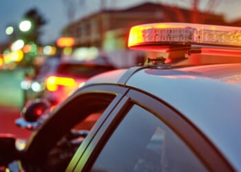 A police car sits alongside a road at night while its lights are flashing.